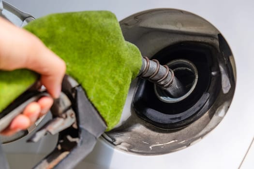 Close up image of hand refilling a car with fuel at a gas station, green fuel nozzle,energy concept