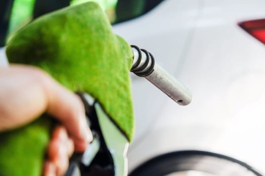 Close up image of hand refilling a car with fuel at a gas station, green fuel nozzle,energy concept