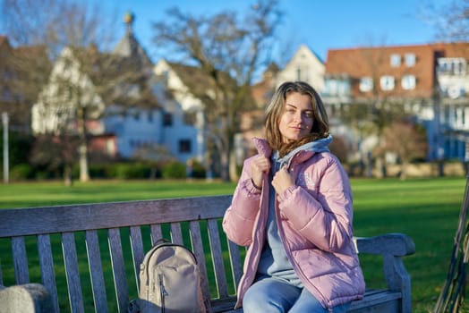 Embrace the tranquility of winter with this captivating image featuring a beautiful girl in a pink winter jacket, leisurely sitting on a bench in a park against the backdrop of a charming old European town. The photograph beautifully captures the serene atmosphere, blending the girl's winter style with the timeless charm of the historic surroundings. Winter Wonderland Elegance: Beautiful Girl in Pink Jacket Enjoys Festive Atmosphere in Bitigheim-Bissingen Park. Experience the magic of the holiday season as a charming girl in a pink winter jacket sits on a bench in a park against the backdrop of the historic town of Bitigheim-Bissingen, Baden-Württemberg, Germany. The scene is adorned with picturesque half-timbered houses, creating a delightful blend of winter charm and architectural beauty.