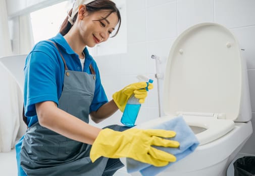 A woman wearing gloves scrubs toilet seat with cloth emphasizing purity in bathroom cleaning. Her meticulous work reflects dedication to housekeeping and hygiene. Housekeeper healthcare concept