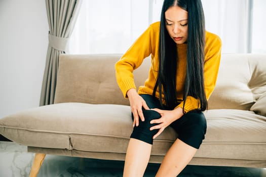 A woman seated on sofa holding a painful knee due to chronic tendon arthritis. Depicting Health Care and Medical Concept highlighting pain and tendon inflammation.