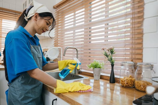Portrait of smiling woman in uniform cleaning kitchen worktop with spray and cloth. Housekeeping emphasizing hygiene and safety. Cleaning routine for a purified home. Clean disinfect home care.