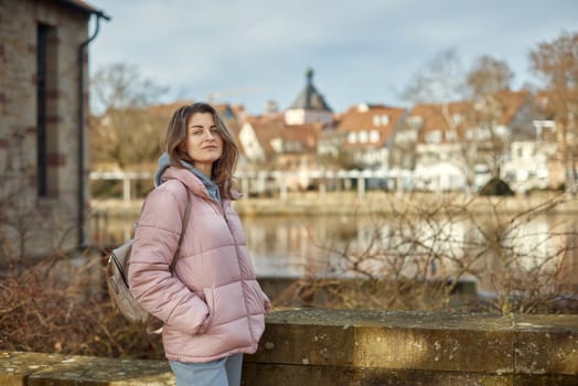 Young beautiful pretty tourist girl in warm hat and coat with backpack walking at cold autumn in Europe city enjoying her travel in Zurich Switzerland. Outdoor portrait of young tourist woman enjoying sightseeing