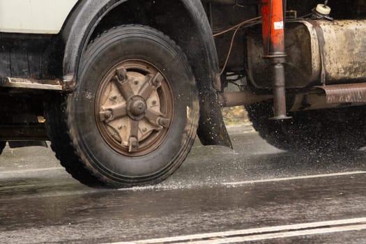 Close up of truck tire rolling on wet asphalt road, with some splashes at rainy day.