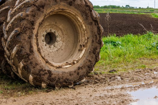 dirty double wheel of a big agriculture tractor on dirt road at summer day, closeup