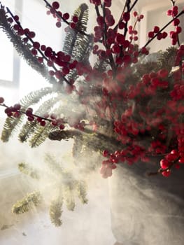 a bouquet of branches with red berries and fir branches in smoke in sunny weather, the rays of the sun through the branches. High quality photo