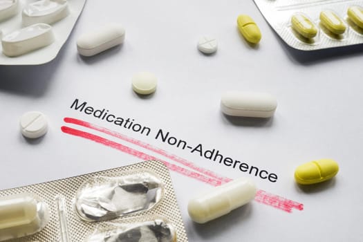 A sheet of paper with inscription Medication non-adherence and pills on it.