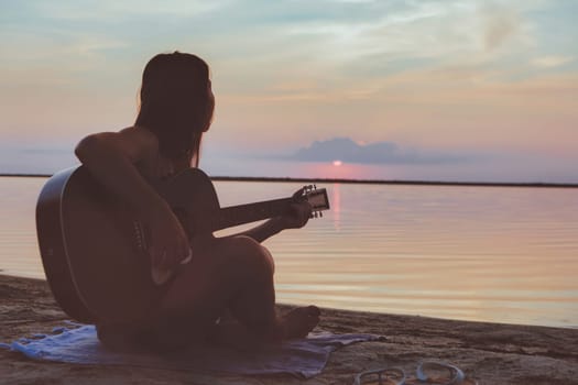 Woman playing guitar on sunset beach