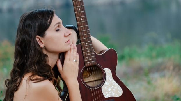 Attractive long haired, looking at the her guitar. Outdoor portrait with nature background, a young and beautiful model. Portrait of young woman with a guitar download