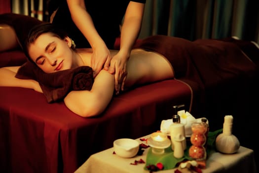 Caucasian couple customer enjoying relaxing anti-stress spa massage and pampering with beauty skin recreation leisure in warm candle lighting ambient salon spa at luxury resort or hotel. Quiescent