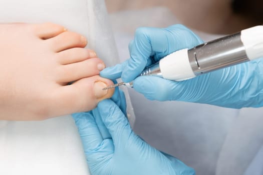 Pedicure expert utilizes an electric drill machine to perform a professional hardware pedicure on female toenails.