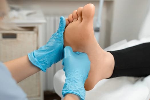 Masseur in rubber gloves is giving a foot massage to a woman.
