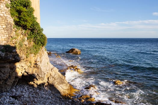 A tranquil seascape with rocky shores, lush greenery, and a clear blue sky