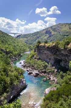 A serene river flows through a dramatic canyon, surrounded by lush greenery and towering rocky cliffs