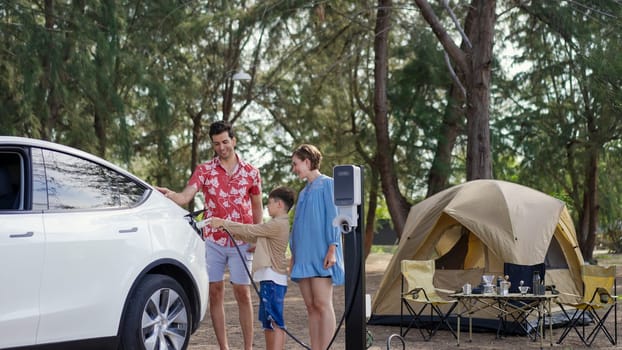 Outdoor adventure and family vacation camping in nature travel by eco friendly car for sustainable future. Lovely family recharge EV car with EV charging station in campsite. Perpetual