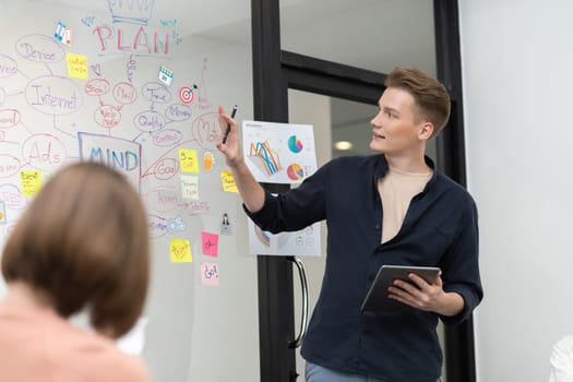 Professional male leader presents start up project by using mind map, colorful sticky notes and business statistic graph with confident while investor listening at business meeting. Immaculate.