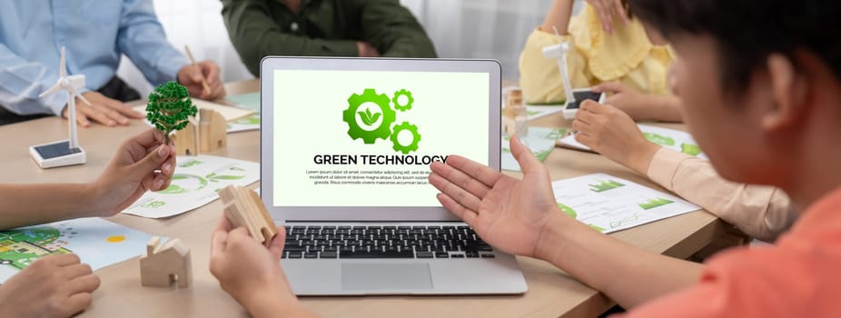 Green technology logo displayed on green business laptop while business team presenting green design to customer. ESG environment social governance and Eco conservative concept. Closeup. Delineation