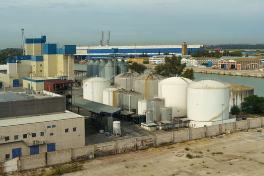 An aerial view capturing the expansive layout of an industrial facility with storage tanks adjacent to a waterfront, under the soft light of the evening sky.