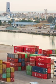 Seville, Spain - June 2, 2023: Multiple colorful shipping containers are neatly stacked at a port terminal, with cranes visible in the background, suggesting active logistics operations.