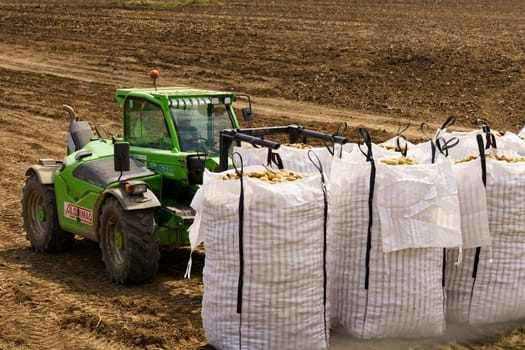 Huevar del Aljarafe, Seville, Spain - June 2, 2023: A tractor pulls a huge sack of potatoes across a dusty field in the countryside.