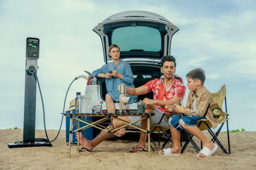 Family vacation trip traveling by the beach with electric car, happy family recharge EV car, enjoying outdoor camping coffee. Seascape travel and eco-friendly car for clean environment. Perpetual