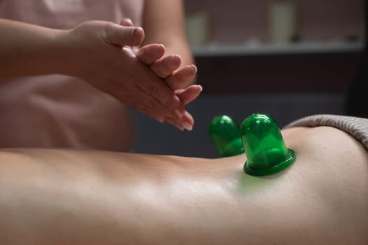 A woman undergoes an anti-cellulite massage procedure using a vacuum jar. Close-up of the lower back