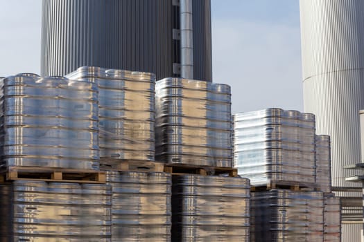 Large amount of aluminium beer kegs stacked on each other with euro palettes and wrapped around with vinyl foil. The beer ready for shipment is bottled in kegs and stored in the yard of the brewery.