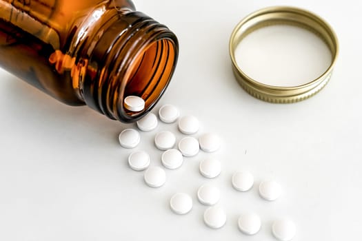 Scattered White Pills and Brown Vial, Close-Up on White Background, Concept of Pharmaceutical