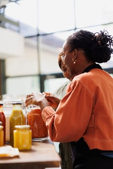 African American vendor in a store, offers advice and serves her customers with freshly harvested, organic bio food. Side view of her interaction with one person in eco friendly local supermarket.