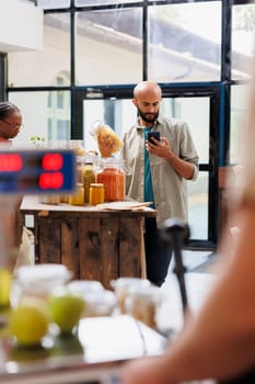 Arab male customer concentrating on his mobile device while clutching the pasta-filled glass jar. Young man provides a modern and effective shopping experience using cellphone.