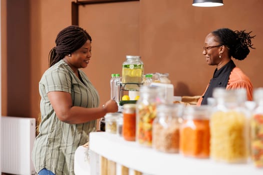 Smiling black woman shops at bio food market, buying fresh organic produce and supporting sustainable practices and zero waste. Female customer preparing to pay for her sustainable products.