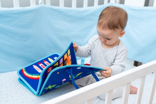 One year old baby playing with montessori busy book sitting in crib