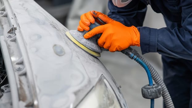 A mechanic sands the putty on a car body with a machine. Repair after an accident