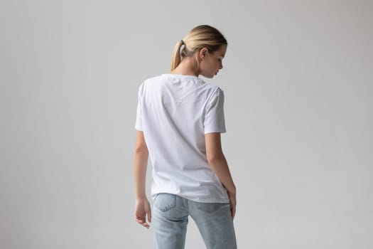 Beautiful blonde woman in a white T-shirt and blue jeans posing on a white background. High quality photo