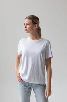 Beautiful blonde woman in a white T-shirt and blue jeans posing on a white background. High quality photo