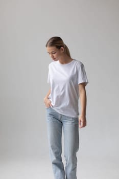 Beautiful blonde woman in a white T-shirt and blue jeans posing on a white background. High quality photo