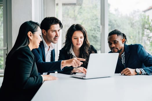 Diverse business professionals, both men and women, work together in meeting room using laptop. Their teamwork, collaboration, diversity are apparent they discuss, plan, and strategize for success.