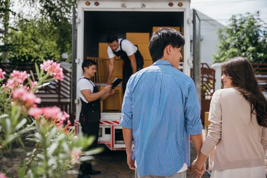 Assisted by a professional delivery team a couple transitions to their new home. Together they unload and lift cardboard boxes ensuring an organized and efficient move. Moving Day Concept