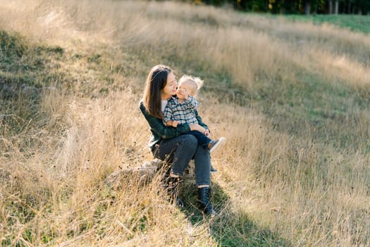 Little girl shows her mother a blade of grass while sitting in her arms in a clearing. High quality photo