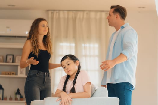 Annoyed and unhappy young girl sitting on sofa trapped in middle of tension by her parent argument in living room. Unhealthy domestic lifestyle and traumatic childhood develop to depression.Synchronos