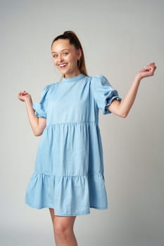 Young happy smiling woman in a light blue dress on a gray background close up