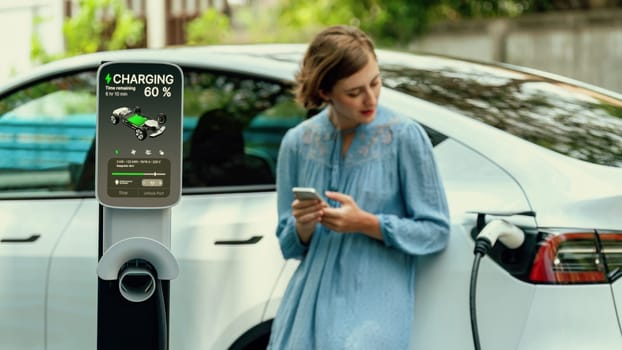 Electric vehicle recharging battery from home EV charging station using alternative energy with net zero emission on blurred background of young girl charging her car before vacation travel. Perpetual