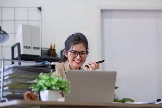 Asian businesswoman or accountant happily sitting and working with laptop on finance and business administration. On the desk in the office decorated with green plants..