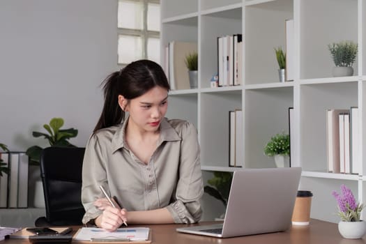 Young Asian business woman sitting in the office using a calculator to calculate business numbers..