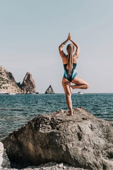 Yoga on the beach. A happy woman meditating in a yoga pose on the beach, surrounded by the ocean and rock mountains, promoting a healthy lifestyle outdoors in nature, and inspiring fitness concept