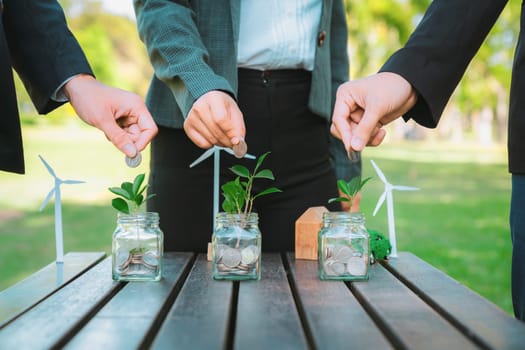 Business people put coin to money saving glass jar on outdoor table as sustainable money growth investment or eco-subsidize. Green corporate promot and invest in environmental awareness. Gyre