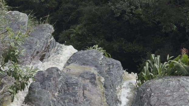 Slow-mo aerial video of water cascading from a verdant waterfall's summit.
