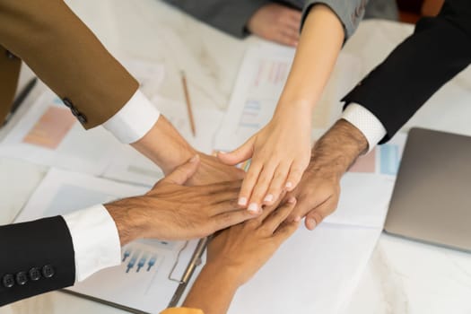 Top view of corporate diverse businesspeople putting hands together on meeting table with document scatter around at business meeting room. Represented unity, cooperation, collaboration. Ornamented.