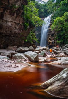 Individual in orange by a tranquil waterfall amidst serene nature.