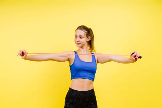 Portrait of gentle muscular woman holding skipping rope on her neck over yellow background